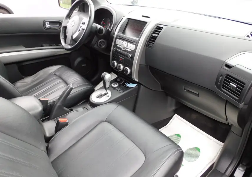 Intérieur noir cuir du Nissan X-TRAIL 2011 vu côté passager, avec tableau de bord et console centrale visibles.