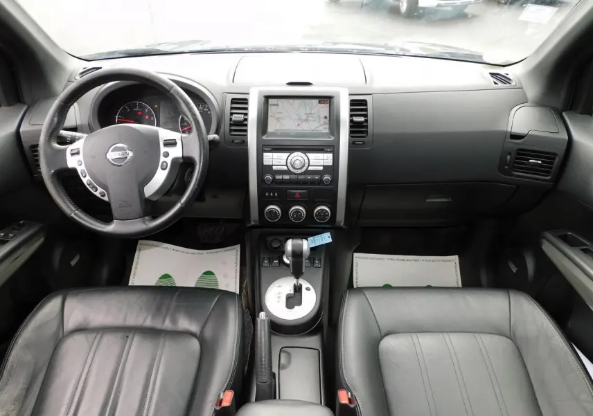 Vue intérieure avant du Nissan X-TRAIL noir de 2011, montrant tableau de bord, volant cuir et console centrale avec écran GPS.