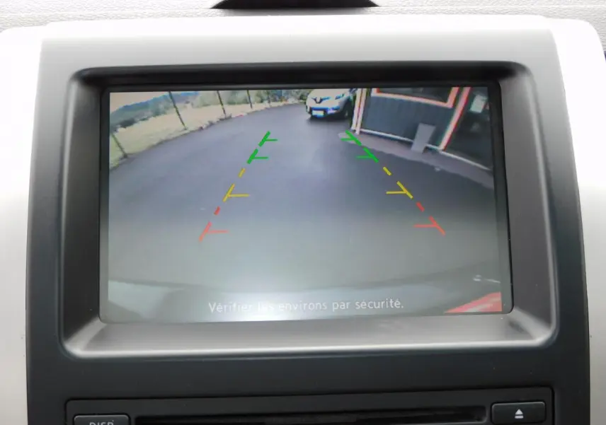 Écran de caméra de recul du Nissan X-TRAIL noir montrant l’arrière avec lignes de guidage colorées et un véhicule blanc en fond.