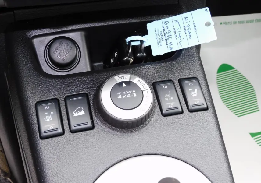 Gros plan sur la console centrale noire du Nissan X-TRAIL 2011, montrant les commandes 4x4 et sièges chauffants.