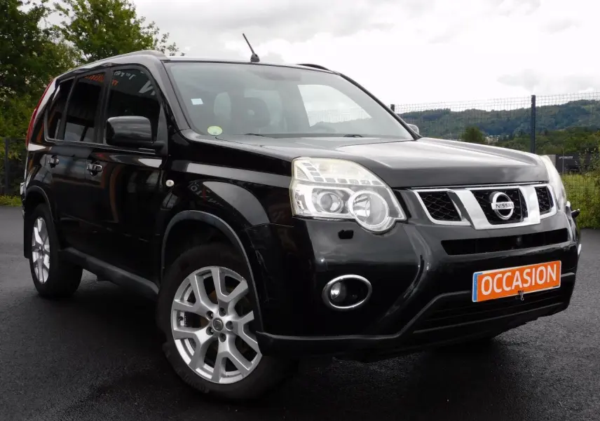 Nissan X-Trail noir vu en 3/4 avant droit sur sol humide avec plaque "OCCASION" orange visible.