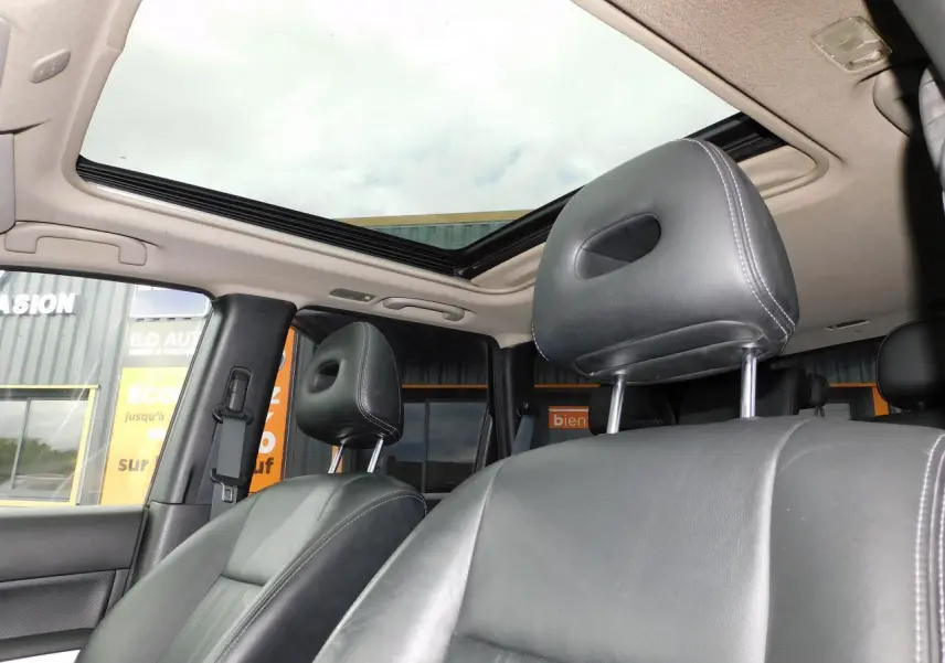 Vue intérieure du Nissan X-TRAIL 2011 montrant les sièges avant en cuir noir et le toit ouvrant panoramique.