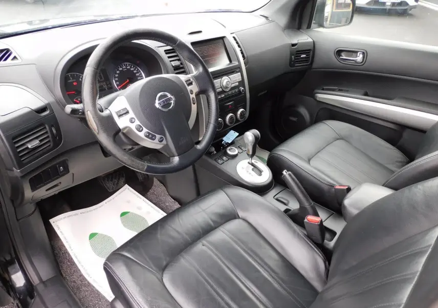 Vue intérieure du Nissan X-TRAIL 2011 montrant les sièges cuir noirs, le volant multifonction et la console centrale avec boîte auto.