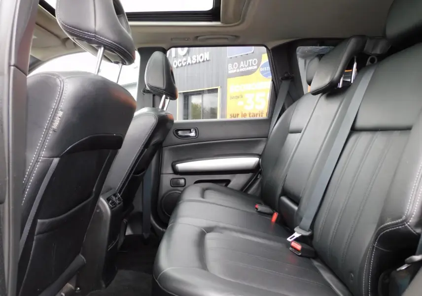 Vue latérale intérieure du Nissan X-TRAIL 2011, sièges arrière en cuir noir sous toit ouvrant panoramique.
