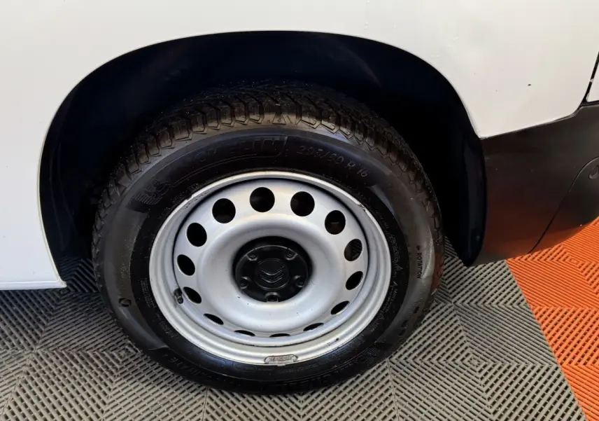 Gros plan sur la roue avant gauche en jante acier du Citroën Berlingo blanc, avec partie de la carrosserie visible.