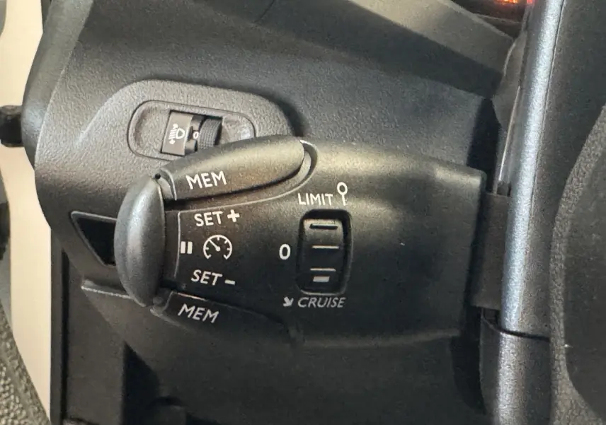 Gros plan sur la commande de régulateur de vitesse noire à gauche du volant dans l’habitacle du Citroën Berlingo blanc.