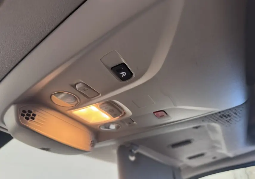 Vue intérieure en plongée sur le plafonnier gris clair du Citroën Berlingo blanc avec éclairage allumé et commandes intégrées.
