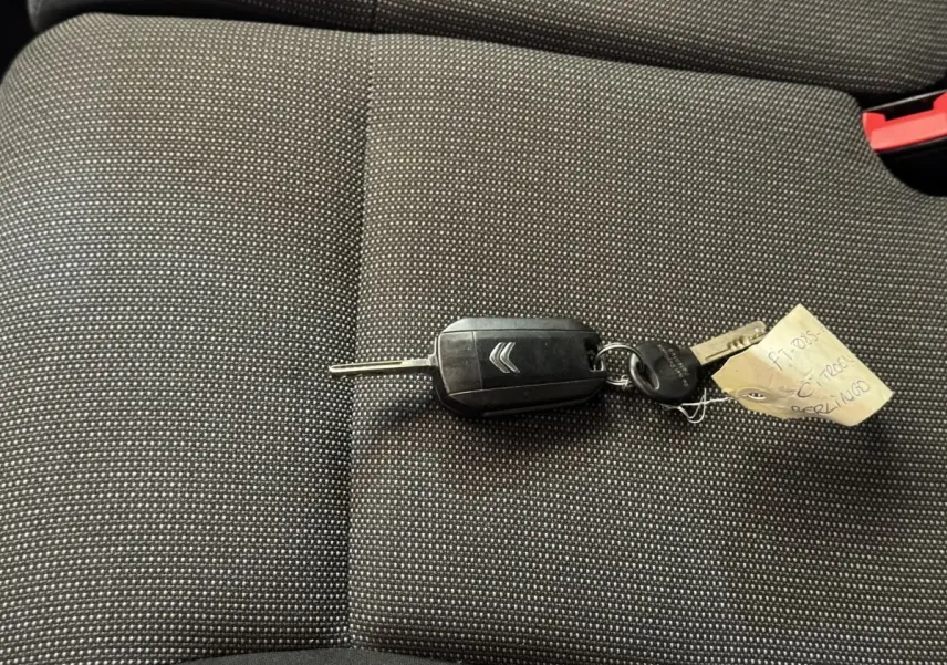 Clé de voiture Citroën posée sur un siège tissu gris foncé à motifs fins, intérieur du véhicule visible en gros plan.