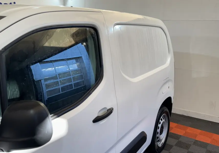 Vue de côté droit arrière d’un utilitaire Citroën Berlingo blanc avec porte latérale pleine et jante acier.
