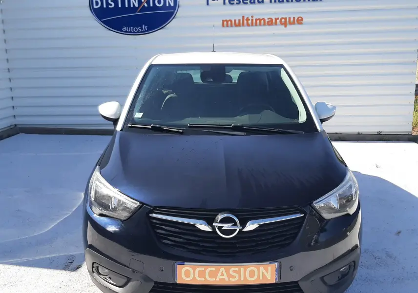 Vue avant d'un Opel Crossland noir avec toit blanc, immatriculé "OCCASION" devant un mur publicitaire.