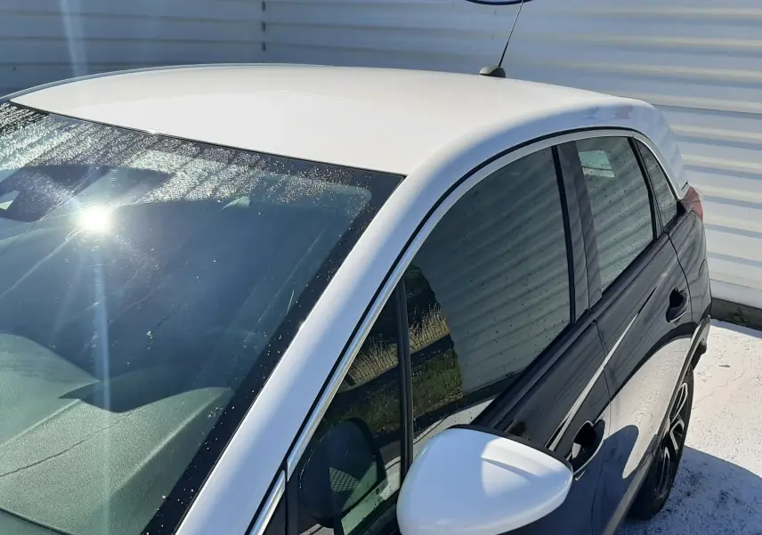 Opel Crossland noir avec toit blanc vu de profil côté gauche, stationné devant un mur blanc avec logo Distinxion.