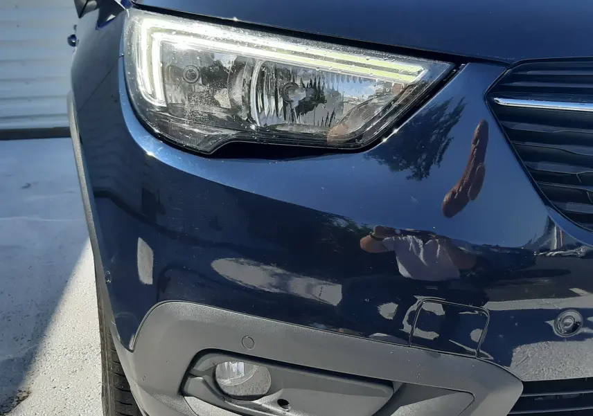 Vue de côté droit en plongée d'un Opel Crossland noir avec toit et rétroviseur blanc, stationné devant un mur publicitaire.