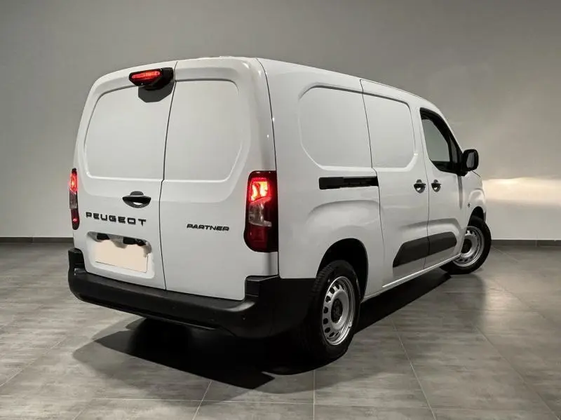 Vue 3/4 arrière droite d'un Peugeot Partner blanc Icy avec portes arrière battantes et feux allumés dans un intérieur neutre.