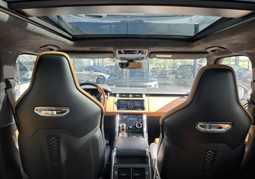 Vue intérieure arrière du Range Rover Sport SVR 2020 avec sièges sport noirs et tableau de bord marron clair sous toit panoramique.