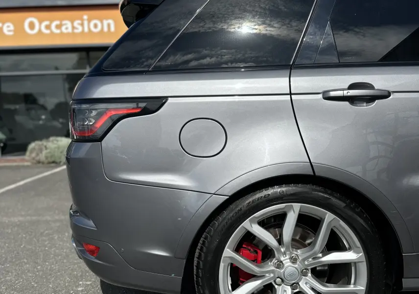 Vue latérale arrière côté gauche d'un Range Rover Sport gris foncé avec jante argentée et étrier de frein rouge.