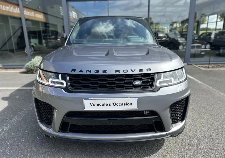 Vue frontale d'un Range Rover Sport gris foncé avec calandre noire et phares LED distinctifs, devant un showroom.