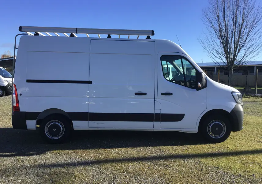 Vue 3/4 arrière droite d'un Renault Master blanc 2020 avec galerie et échelle métallique sur la porte arrière.