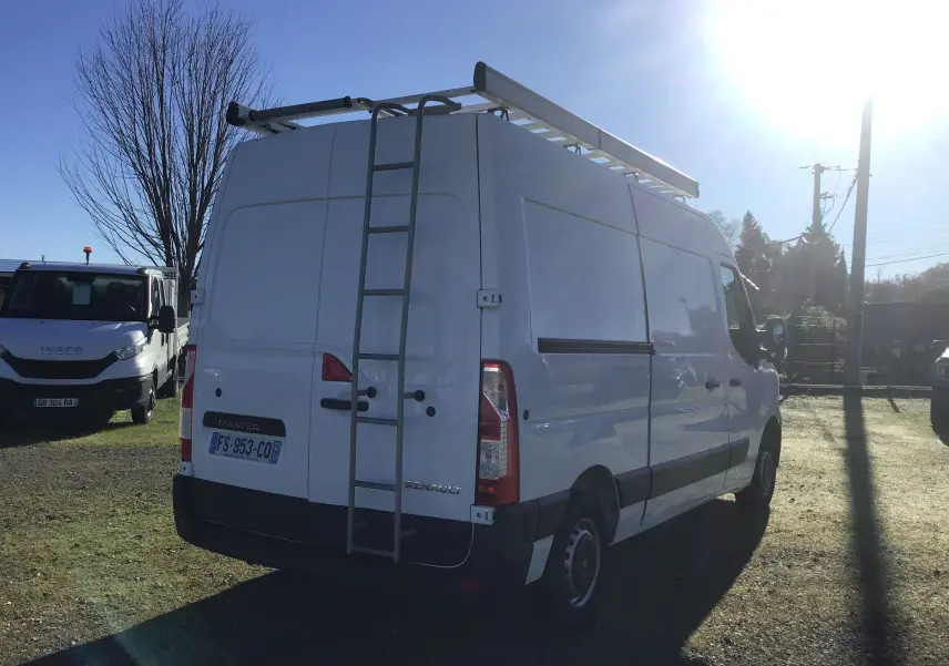 Vue arrière d'un Renault Master blanc avec échelle métallique fixée sur la porte droite et galerie de toit visible.
