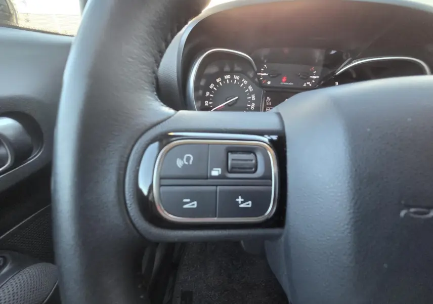 Gros plan sur les commandes audio au volant cuir noir du Citroën C3 Aircross 2021, tableau de bord en arrière-plan.