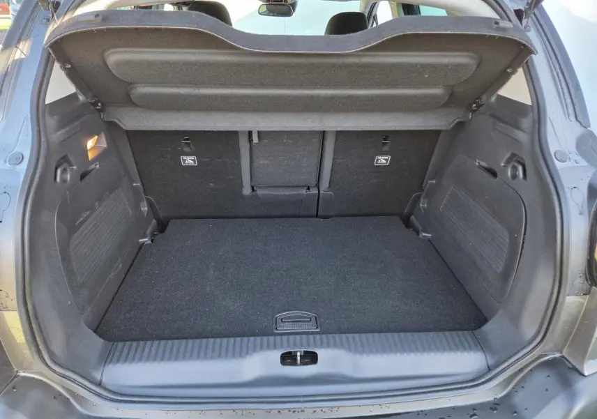 Coffre ouvert vu de l'arrière d'une Citroën C3 Aircross gris platinium avec intérieur noir et banquette rabattue partiellement.