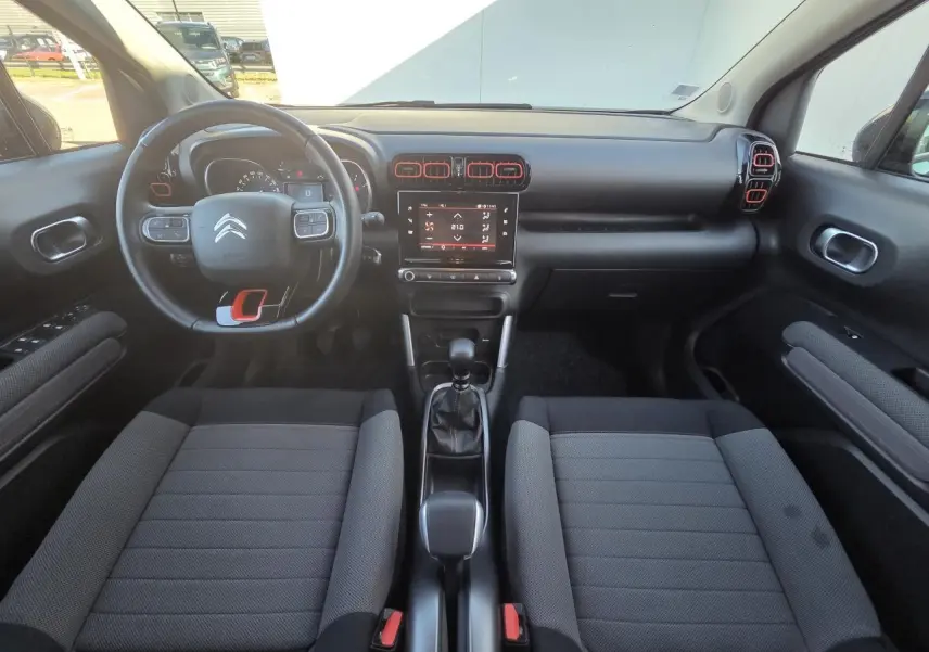 Intérieur avant du Citroën C3 Aircross 2021, tableau de bord noir avec touches rouges et sièges tissu gris foncé.