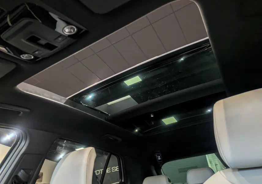 Vue intérieure du toit ouvrant panoramique du Kia Sportage 2025 gris céramique avec sièges cuir clair et plafond noir.