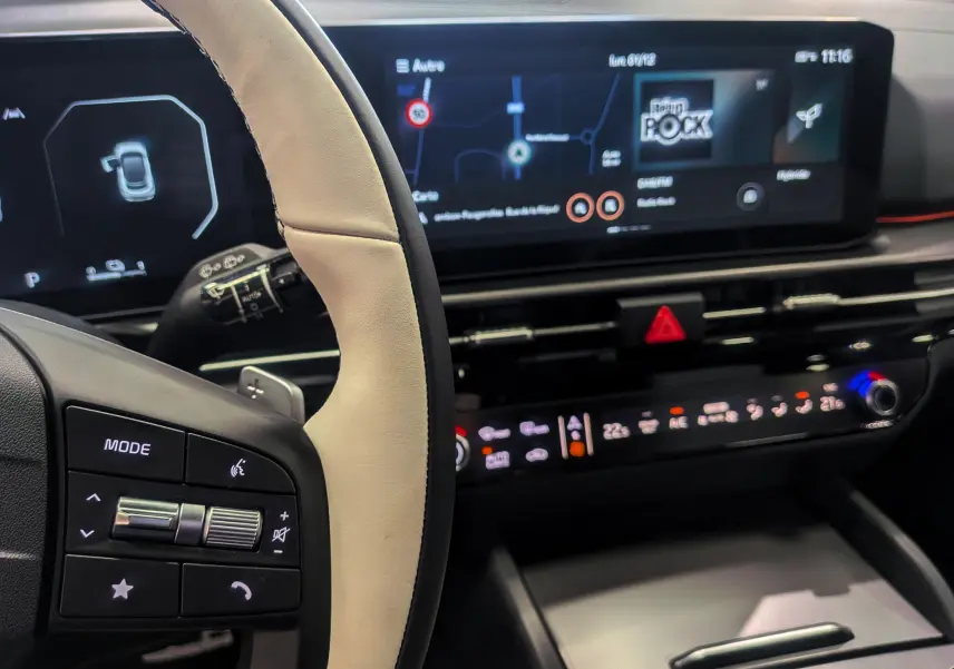 Vue rapprochée du tableau de bord et volant cuir clair du Kia Sportage hybride 2025 avec écran tactile et commandes intégrées.