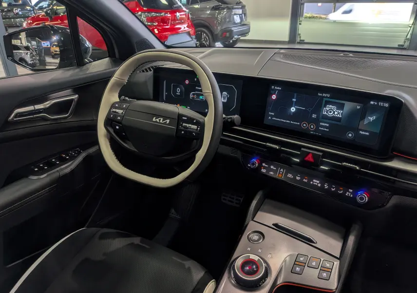 Vue intérieure côté conducteur du Kia Sportage 2025 hybride, volant cuir clair et tableau de bord numérique moderne.