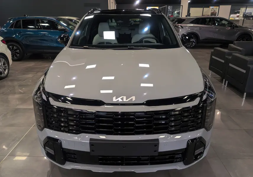 Vue frontale d'un KIA SPORTAGE 2025 gris céramique avec toit noir et calandre noire brillante en showroom.