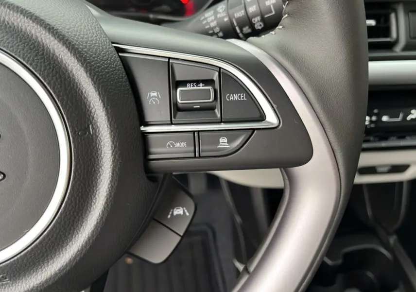 Gros plan sur le volant cuir multifonctions de la Suzuki Swift 2025, avec commandes de régulateur de vitesse et assistance au maintien de voie.