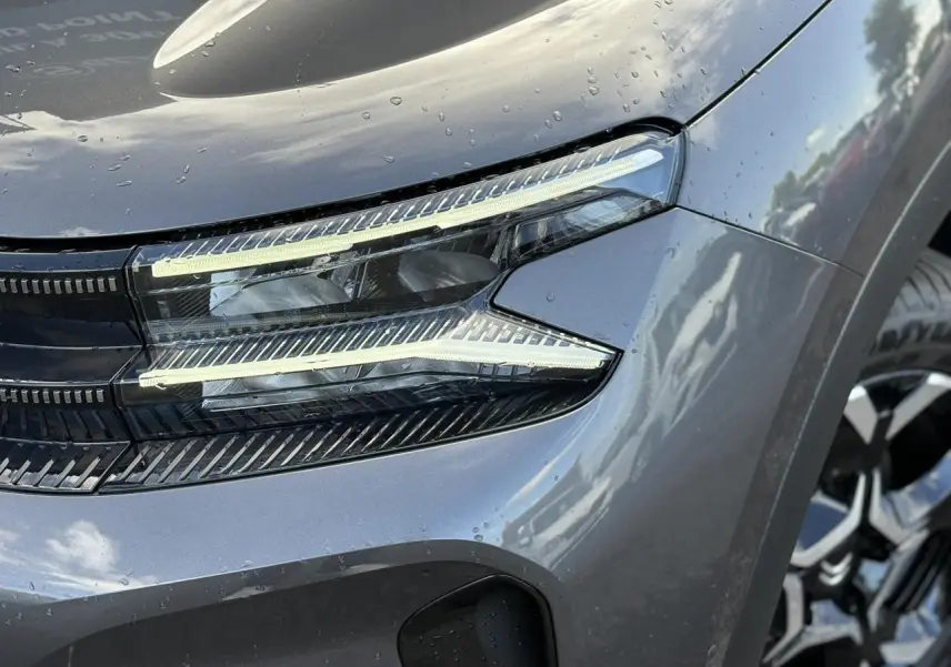 Gros plan sur le phare avant droit du Citroën C5 Aircross gris Platinium avec jante alliage visible.