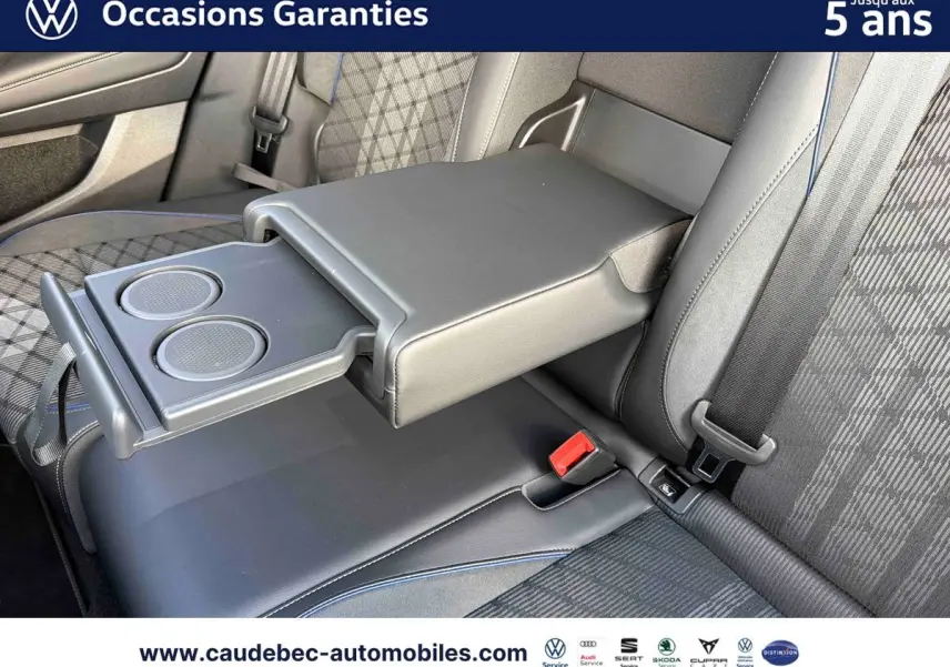 Vue rapprochée de l'accoudoir central arrière déployé avec porte-gobelets du Volkswagen Tiguan 2025, sellerie noire à motifs.