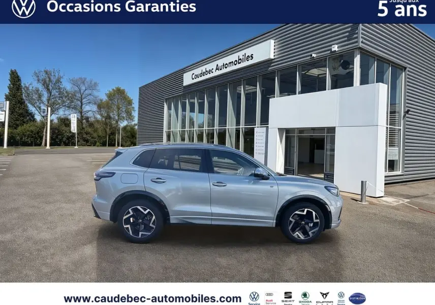 Vue latérale droite d'un Volkswagen Tiguan 2025 argent Dolomite avec jantes alliage et toit panoramique, devant un concessionnaire.