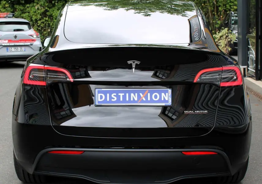 Vue arrière d'une Tesla Model Y noire métal 2024 avec logo "Dual Motor" et plaque Distinxion visible.