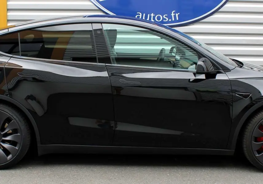 Tesla Model Y noir métal vue de profil côté gauche, avec jantes noires et étriers de frein rouges visibles.
