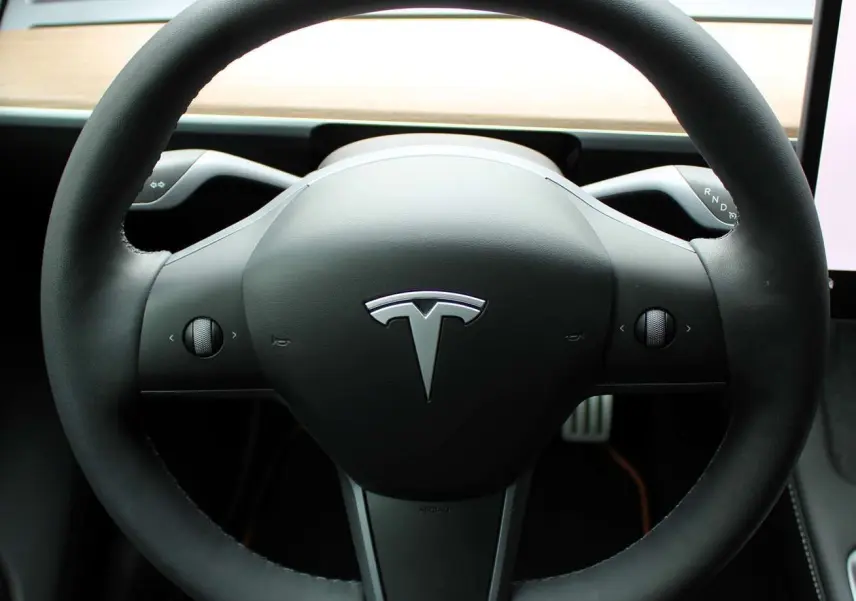 Gros plan sur le volant noir de la Tesla Model Y 2024 avec tableau de bord en bois clair en arrière-plan.