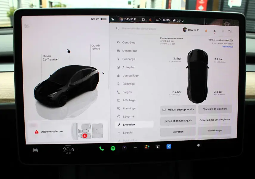 Écran tactile du tableau de bord d'une Tesla Model Y noire métal 2024 montrant l'état des pneus et options d'entretien.