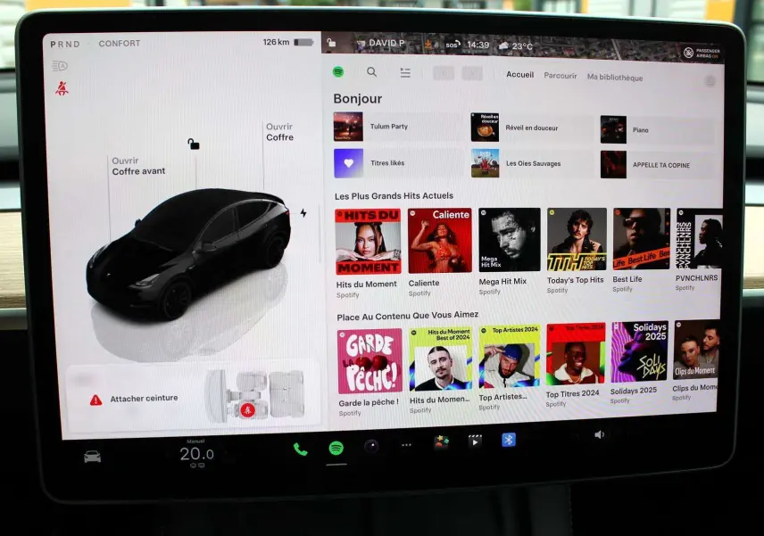 Écran tactile central affichant une Tesla Model Y noire en vue 3/4 avant avec commandes et musique Spotify visible.