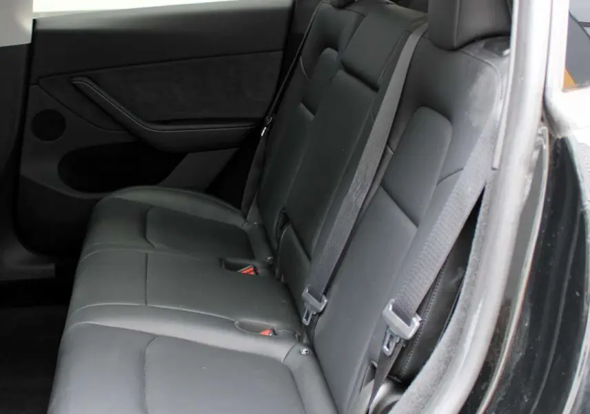 Vue latérale droite de l'intérieur arrière du Tesla Model Y 2024 noir métal avec sièges en cuir noir et ceintures de sécurité.
