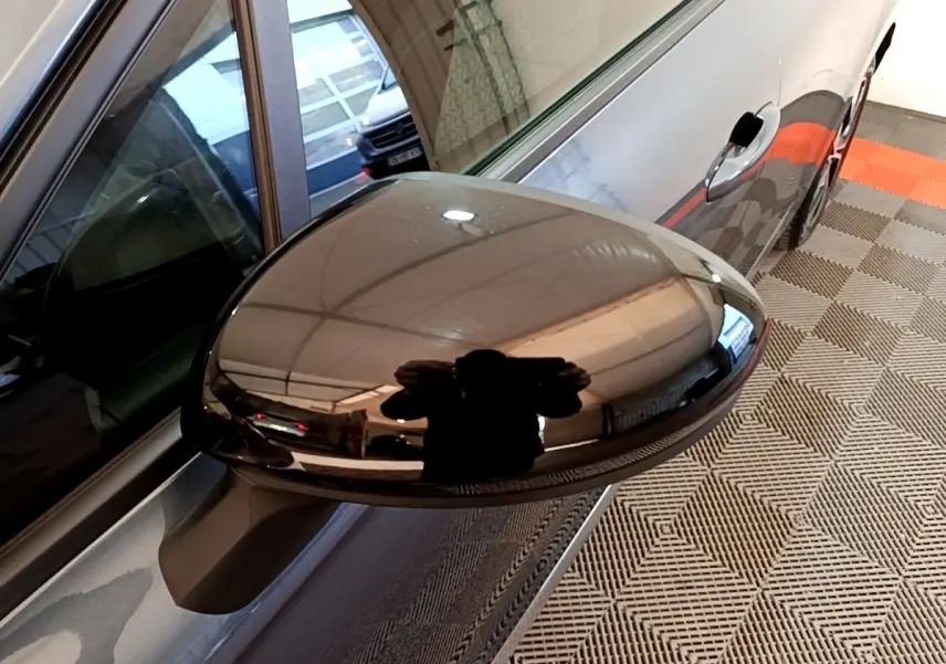 Gros plan sur le rétroviseur droit noir brillant d'une Renault Clio gris foncé, vue latérale en intérieur.