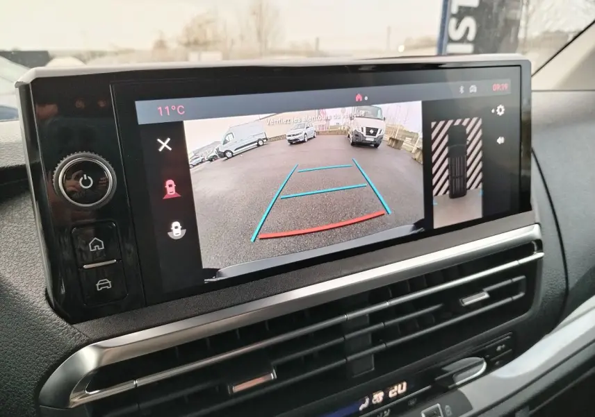 Écran central du tableau de bord montrant la caméra de recul avec vue arrière sur un parking, intérieur noir.