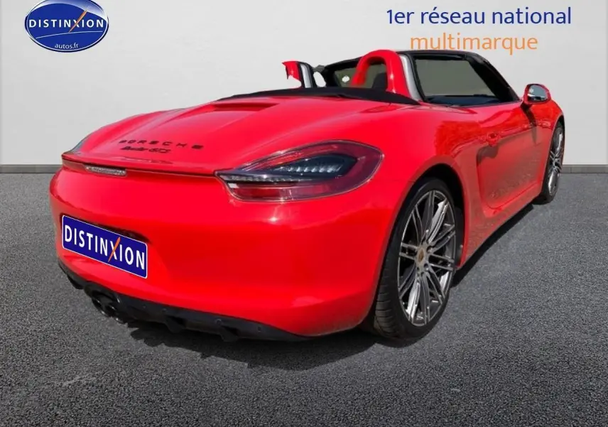 Vue 3/4 arrière droite d'une Porsche Boxster rouge cabriolet avec jantes alu et becquet arrière.