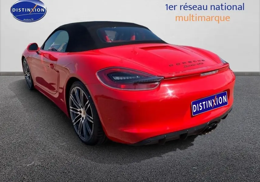 Vue 3/4 arrière droite d'une Porsche Boxster GTS rouge avec capote noire et jantes alu multibranches.
