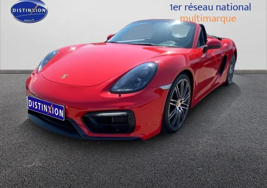 Vue 3/4 avant droite d'une Porsche Boxster 981 rouge avec jantes alu et capote ouverte sur fond neutre.