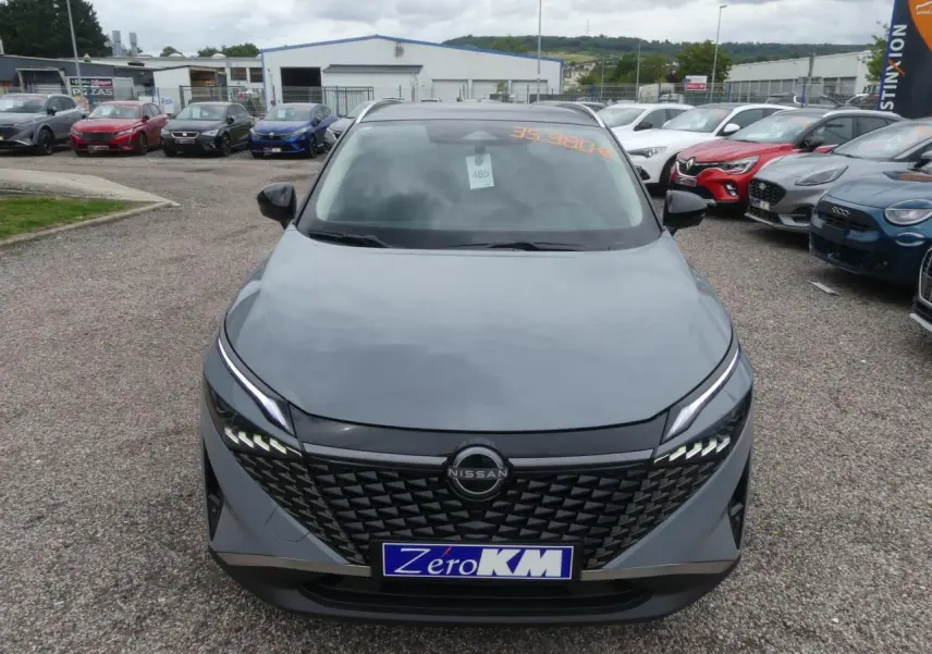 Vue avant d'un Nissan Qashqai gris métallisé avec calandre noire et feux LED distinctifs sur un parking.