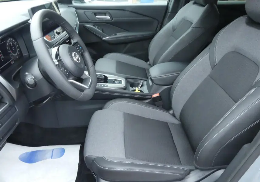 Vue intérieure côté conducteur du Nissan Qashqai 2025 avec sièges tissu gris et volant cuir noir.