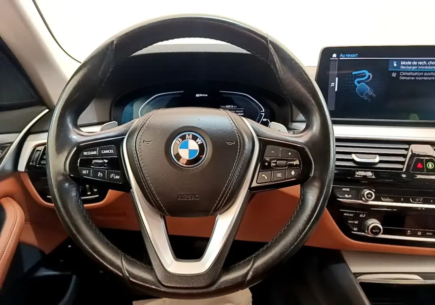 Vue intérieure centrée sur le volant cuir noir et le tableau de bord marron de la BMW Série 5 Touring 530e hybride rechargeable.