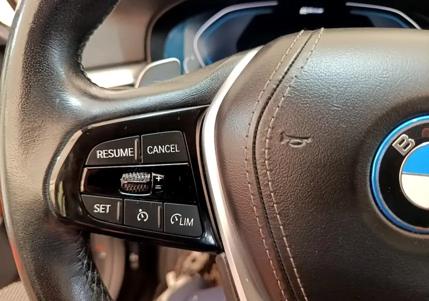 Gros plan sur le volant cuir noir de la BMW Série 5 Touring 530e, avec commandes de régulateur de vitesse à gauche.