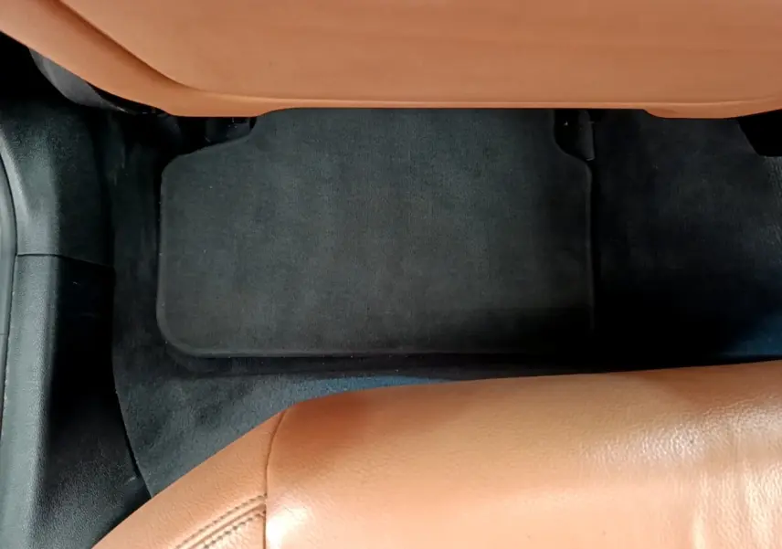 Détail du sol arrière avec tapis noir et sellerie cuir marron clair dans une BMW Série 5 Touring 530e hybride 2022.