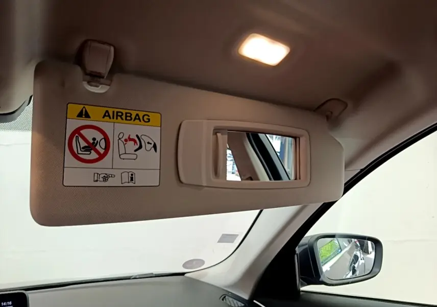 Détail du pare-soleil côté conducteur beige avec miroir intégré et étiquette airbag dans une BMW Série 5 Touring gris clair.